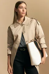 Trench color beige de corte clásico con cuello amplio, botones frontales, detalles en los hombros y mangas largas.