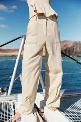 Pantalón de tiro alto color beige confeccionado con lino, de pierna recta, con bolsillos delanteros y falsos bolsillos de vivo en la espalda.