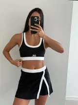 Conjunto deportivo negro con detalles en blanco, compuesto por un top con logo y una falda corta cruzada.