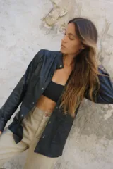 Camisa negra de cuero ovino con cuello mao, cierre frontal con botones a presión, dos bolsillos de parche en el pecho y tachas doradas en cuello, bolsillos y puños.