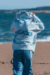 Hoodie celeste con capucha y cordones ajustables, con bordado de la frase "Glassy Waves" en el pecho y un diseño de olas en la manga.