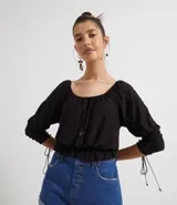 Blusa de poliéster negra con mangas largas abullonadas, escote redondo con botones y bordado en el frente. Tiene volados en el ruedo y ajuste con lazos en los laterales.