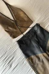 Top marrón de cuero ovino vintage con cuello halter y espalda descubierta. Presenta detalle artesanal de cutouts y pasamanería en negro alrededor del cuello y lazos finos negros para atar en el frente.