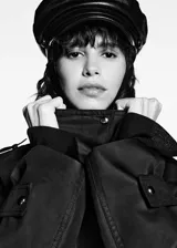 Anorak negro oversize con cuello alto, cierre frontal con botones y cremallera oculta, dos bolsillos laterales con cremallera, mangas largas con puños abotonados y charreteras en los hombros.