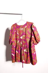 Blusa de calce holgado con estampado floral en tonos marrones, fucsias, naranjas y blancos. Escote en V con doble lazo ajustable y mangas 3/4 con volumen.