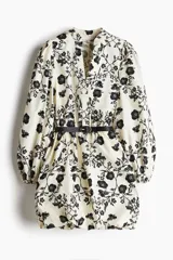 Vestido corto de algodón color crema con estampado floral negro, cuello mao, escote en V, mangas globo con puños elásticos, falda balloon y cinturón extraíble con hebilla ovalada.