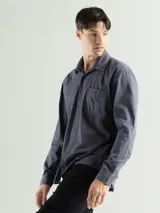 Camisa de manga larga color verde oliva, confeccionada en algodón. Tiene corte clásico, bolsillo en el lado izquierdo del pecho y cierre con botones.