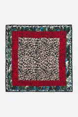 Pañuelo cuadrado con diseño de múltiples estampados animales en capas concéntricas. El centro presenta un estampado de leopardo en tonos rosa pálido y verde/negro. Le sigue un borde rojo con estampado de dálmata/leopardo pequeño, luego un borde verde con estampado de piel de serpiente, y finalmente un borde exterior con estampado de piel de serpiente en tonos blanco, negro y turquesa.