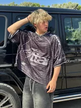 Camiseta negra con estampado de logos en gris y blanco, cuello redondo y mangas cortas. Diseño con ribetes blancos en cuello y mangas.