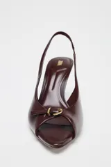Zapato tipo sandalia destalonada color marrón chocolate, con tacón fino, tira delantera con detalle de hebilla metálica dorada y tira trasera elástica.