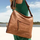 Cartera de cuero color marrón claro, con bolsillo frontal con tapa y cierre. Incluye división interna, bolsillos internos y bolsillo trasero con cierre. Tiene correa larga regulable y asa de mano.