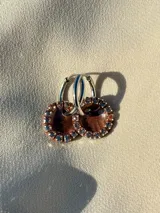 Par de aros colgantes con argolla de acero quirúrgico, dije circular de resina negra y borde de strass plateado.