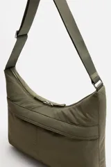 Bolso de hombro color verde oliva, fabricado en tejido técnico acolchado. Tiene un compartimento principal con cierre de cremallera, un bolsillo interior con cremallera y un bolsillo frontal con cremallera. El asa de hombro es ajustable.