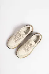 Zapatillas deportivas color beige con detalles en marrón y amarillo.