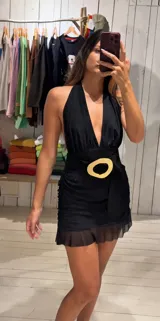 Vestido corto negro de microtul con escote halter profundo y frunces en el torso. Presenta un cinturón ancho negro con hebilla circular grande en tono dorado claro, y falda corta con volados de tul transparente en el ruedo.