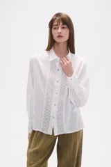 Camisa blanca de broderie con cuello camisero, cierre frontal de botones, mangas largas y corte holgado.