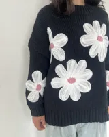 Sweater tejido negro con cuello redondo y tres flores blancas bordadas en el frente.