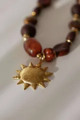 Collar corto con cuentas de madera color marrón en diferentes tonos, detalles dorados y dije de sol dorado con diseño grabado.