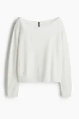 Buzo de punto fino color blanco, con escote amplio tipo barco que deja los hombros descubiertos, manga larga y puños y bajo acanalados.