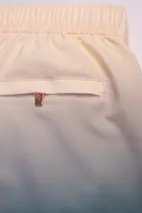 Short de baño con degradé de color beige a azul, con cintura elástica y cordón ajustable. Tiene protección UV50, logo de la marca, dos bolsillos laterales y uno trasero con cierre.