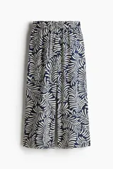 Pantalón tobillero cropped de viscosa con estampado de hojas en color crema sobre fondo azul marino. Tiene tiro alto con elástico en la cintura, bolsillos laterales y piernas amplias rectas.
