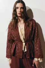 Kimono color ladrillo con bordado floral, confeccionado en lino. Tiene mangas largas, cinturón ajustable con lazadas y detalle de abalorios.