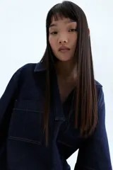Vestido corto de denim azul oscuro, corte recto, con cuello camisero con escote en V, manga corta y dos bolsillos de parche en el pecho.