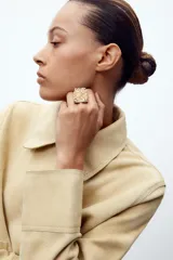 Anillo metálico rectangular con diseño de pequeños cuadrados dorados sobre base plateada.