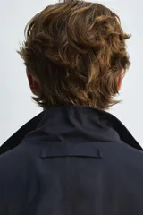 Parka azul marino de tejido técnico, corte relaxed fit, cuello alto ajustable con cordón, manga larga con puños abotonados, cierre frontal con cremallera oculta y solapa con botones a presión, cintura ajustable con cordón interior y bolsillos frontales multifunción de plastrón.