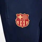 Pantalón largo de fútbol Nike FC Barcelona Strike para hombre, color azul marino con detalles en naranja. Presenta el escudo del club y el logo de Nike bordados.