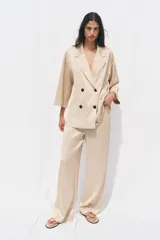 Blazer color beige de cuello solapa y manga tres cuartos. Tejido con efecto arrugado y cierre frontal cruzado con botones negros.