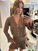 Blusa de lino color marrón, con escote en V adornado con volados y botones de nácar. Las mangas largas terminan en puños con volados.