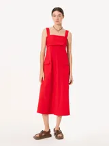 Vestido midi rojo de poplin con lycra, corte evasé, breteles anchos, bolsillos laterales y tajo frontal. Se ajusta en la espalda con un lazo.