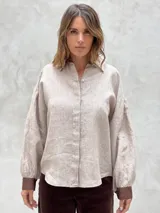 Camisa beige a rayas verticales finas, con cuello clásico, mangas largas abullonadas con puños marrones y cierre frontal con botones.