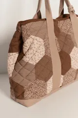 Bolso tipo tote amplio, confeccionado en patchwork de hexágonos con diferentes estampados en tonos azul marino y blanco/gris. Presenta asas y base en tela lisa gris. El cuerpo del bolso tiene un efecto acolchado.