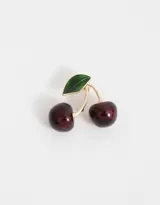 Pin prendedor con forma de cerezas esmaltadas en color rojo oscuro con hoja verde y detalles dorados.