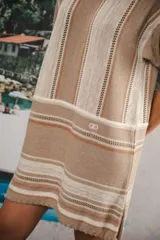 Vestido corto tejido color crudo con rayas verticales marrones y celestes. Tiene cuello redondo y mangas cortas con terminaciones en color rojo.