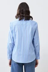 Camisa celeste con rayas verticales blancas, de manga larga y corte clásico, con cuello camisero y dos bolsillos con solapa en el pecho.