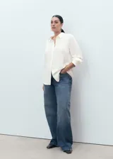 Camisa blanca de manga larga con puños abotonados, cuello camisero y cierre frontal de botones. Diseño recto con tejido fluido.