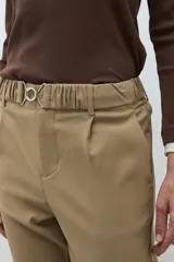 Pantalón negro de vestir, corte recto y tiro alto, con pliegues frontales y puños doblados. Se complementa con un cinturón fino negro con hebilla metálica en forma de símbolo.