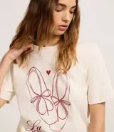 Remera color crudo de algodón, con cuello redondo y mangas cortas. Estampa frontal con dibujo de zapatillas de ballet, corazón y texto "La Coquette avec tout mon amour".