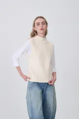 Chaleco de punto color crema, sin mangas, con cuello alto y textura acanalada vertical.