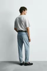 Jeans de denim de algodón, color negro lavado, con tiro medio, corte ajustado en cadera y muslos, y pierna que se estrecha hacia el tobillo. Presenta cinco bolsillos y cierre frontal con cremallera y botón.