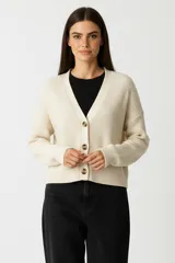Cardigan de punto acrílico color crema, con cuello en V, manga larga y botones frontales. Presenta un tejido acanalado grueso y un calce holgado.