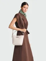 Bolso tipo bucket XS de cuero color crema, con asa corta y correa larga extraíble. Cierre con broche metálico plateado.