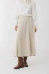 Falda midi color beige de tejido de punto acanalado, con corte evasé y terminación con puntada overlock en color rojo.