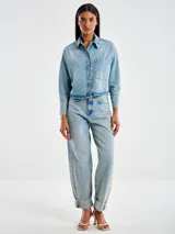 Chaqueta camisera de denim celeste, corta por delante y más larga por detrás, con cierre frontal con botones y bolsillo frontal aplicado en el pecho.