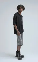 Camisa de manga corta tejida en punto abierto negro, con cuello polo y cierre frontal de botones. Presenta un calce oversize.
