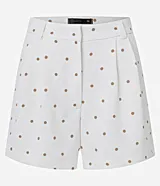 Bermuda de piquet color blanco con estampado de lunares negros, de corte recto, tiro alto, con trabillas en la cintura, pliegues y cierre tradicional.