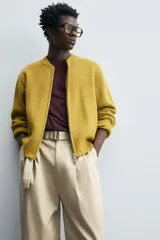 Chaqueta de punto color mostaza, corte relaxed fit, con cuello elástico, manga larga, bolsillos en la cadera, acabados en rib y cierre frontal con cremallera.